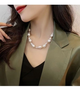 Close-up of baroque pearl necklace with gold beads worn on neck against green suit