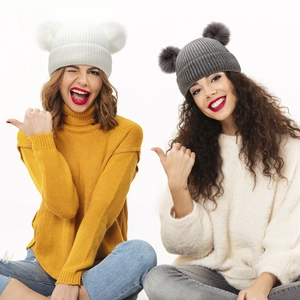 Detail of white and grey knitted beanie hats with fluffy double faux fur pompoms