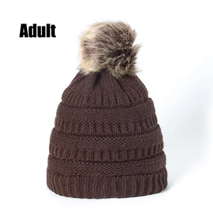 Detail of dark brown knit beanie with thick texture and fluffy faux fur pompom for adults