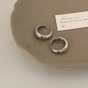 Detailed view of polished chunky silver hoop earrings on a beige ceramic tray