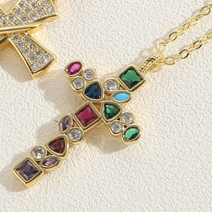 Macro detail of gold cross pendant necklace featuring colorful zircon stones and O-chain