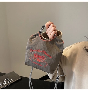 Close-up of dark grey nylon mini bag with red cherry embroidery and checkered strap