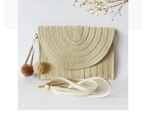Detail of straw woven envelope clutch with pompom bag charm and adjustable PU strap