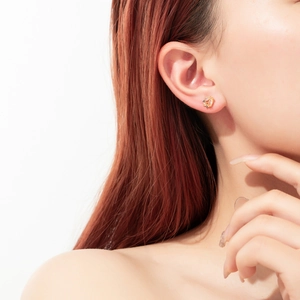 Close-up of elegant gold stud earrings with colorful zircon stones on model's ear