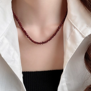 Detailed view of deep red gravel beaded necklace worn by a model on a white shirt