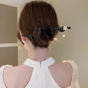 Detail of wooden hair stick with white pearl flower accent on an elegant bun hairstyle