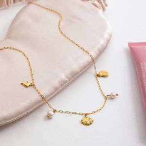 Macro shot of gold necklace with dolphin, shell and pearl charms on pink silk