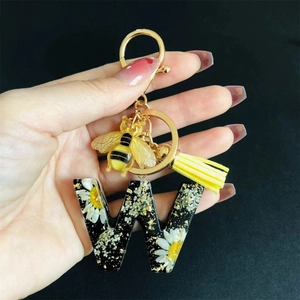 Detail of resin letter W keychain with white daisy flowers, gold flakes and bee charm