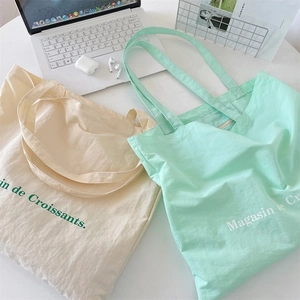 Detailed view of beige and mint green nylon tote bags with Magasin de Croissants print