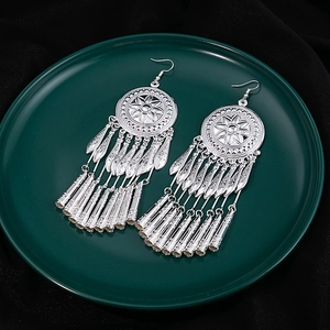 Detail view of silver bohemian tassel earrings on green disc over black velvet backdrop