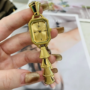Dettaglio di un orologio al quarzo rettangolare dorato con logo Tt tenuto in mano