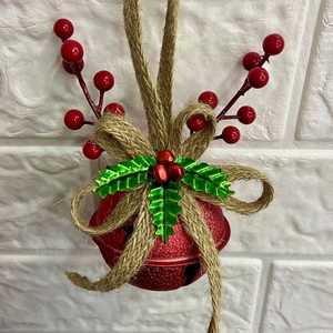 Rustic red Christmas bell with burlap bow and holly berries hanging on a white wall