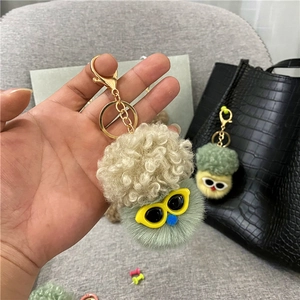 Close-up of green plush cauliflower keychain with yellow glasses on black leather bag