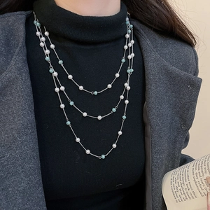 Dettaglio della collana a tre strati con perle e cristalli su un maglione nero raffinato