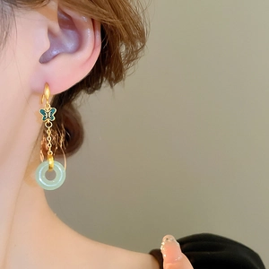 Détail de boucles d'oreilles dorées avec papillon vert et anneau en jade imitation