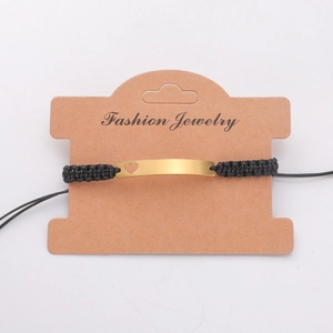 Close-up of hand-woven black cord bracelet with a curved gold heart bar on a card
