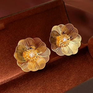 Macro shot of gold floral earrings with crystal center and brushed metal detail