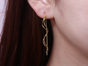 Detail shot of elegant long gold spiral ear threads worn by model showing metal luster