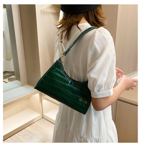 Detail view of a dark green crocodile pattern shoulder bag worn by a model in a dressing room
