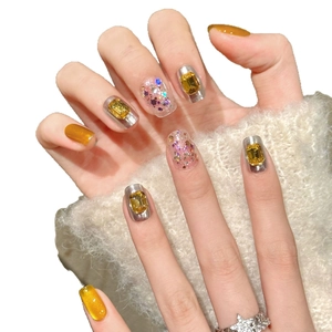 Unghie finte glitterate dorate con gemme gialle e paillettes rosa su maglione bianco