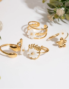 Detail of four adjustable gold-plated rings with white flower designs and crystals