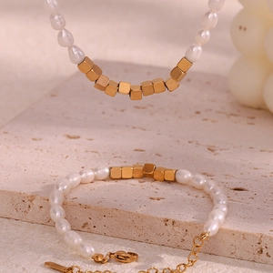 Elegant gold square beads and white freshwater pearl necklace set on beige stone background