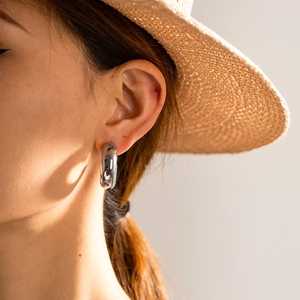 Polished silver chunky hollow C-shaped hoop earrings worn by a model in sunlight