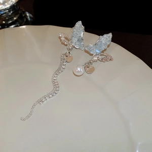Macro detail of asymmetric silver butterfly earrings with crystals and pearl drops
