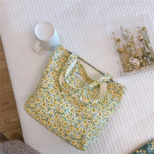 Floral cotton tote bag with zipper and handles on a white quilted fabric surface