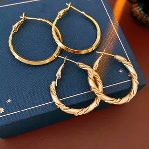 Close-up of golden smooth and twisted hoop earrings on a blue star-patterned jewelry box