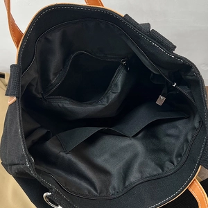 Large black canvas tote bag with brown handles showing spacious interior and zipper pockets