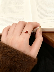 Detail of wulu ring with red enamel and white stones worn on model hand over a book