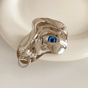Close-up of a silver liquid metal brooch with a realistic blue eye and rhinestones