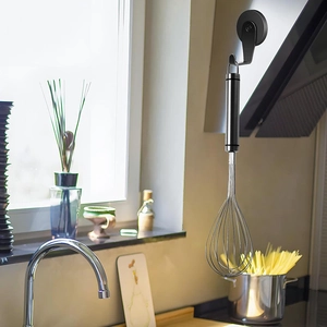 Close-up of a stainless steel whisk hanging on a strong magnetic hook in a bright kitchen
