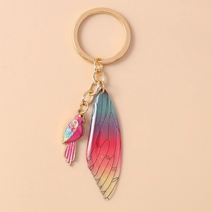 Detailed close-up of colorful enamel parrot and butterfly wing pendants on a gold keychain