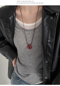 Detail showing the deep red oval pendant on a matching cord necklace worn by a model