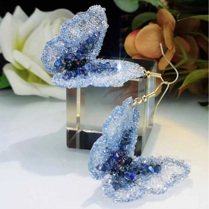 Sparkling blue crystal butterfly earrings with gold hooks on a bright floral display