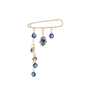 Detail of gold safety pin brooch with blue evil eye beads and silver Hamsa hand charms