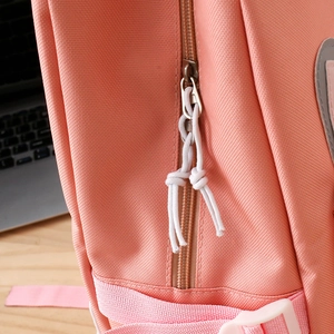 Detailed close-up of coral pink backpack front pocket with white cord zipper pull