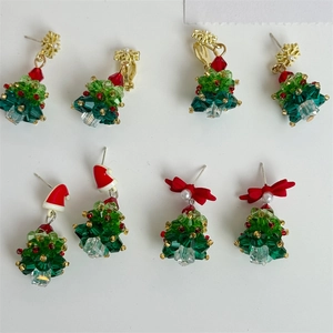 Detailed close-up of handmade beaded Christmas tree earrings with red bows and crystals