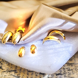 Detail shot of 18K gold teardrop earrings and studs on a luxurious silk background