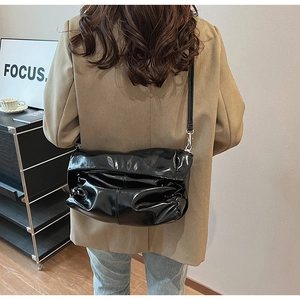 Dettaglio di una borsa a tracolla nera lucida a pieghe indossata su un blazer kaki