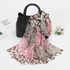 Detail of leopard print and pink gradient chiffon scarf draped on a black leather handbag