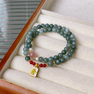 Detail of beaded wrap bracelet featuring green stones and a gold lucky charm pendant