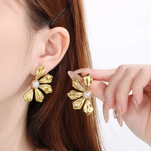 Model wearing golden flower stud earrings with a pearl center and detailed petal texture