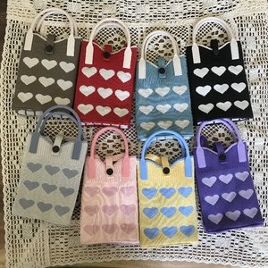 Knitted heart pattern handbags in eight vibrant colors displayed on a lace surface