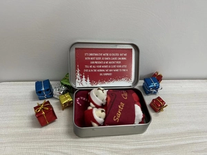 Christmas gift set with red teddy bear socks, silver tin box, and greeting card on wood