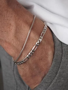 Close-up of layered silver chain bracelets in thick and thin styles on male wrist