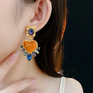 Close-up of vintage gold earrings with heart-shaped orange gem and colorful crystals