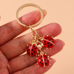 Detail of three red ladybug charms on a gold metal keychain with a pink background